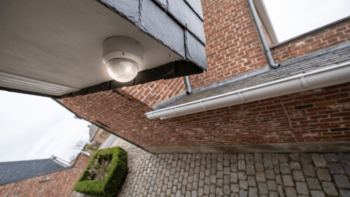 Compacte koepelcamera onder de dakgoot van een bakstenen rijwoning in een Belgische woonstraat