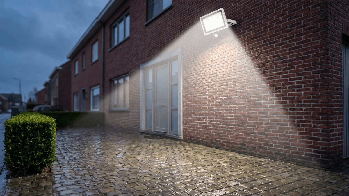 Een breedstraler op de bakstenen gevel verlicht bij schemering de volledige
oprit van een Belgische rijwoning.