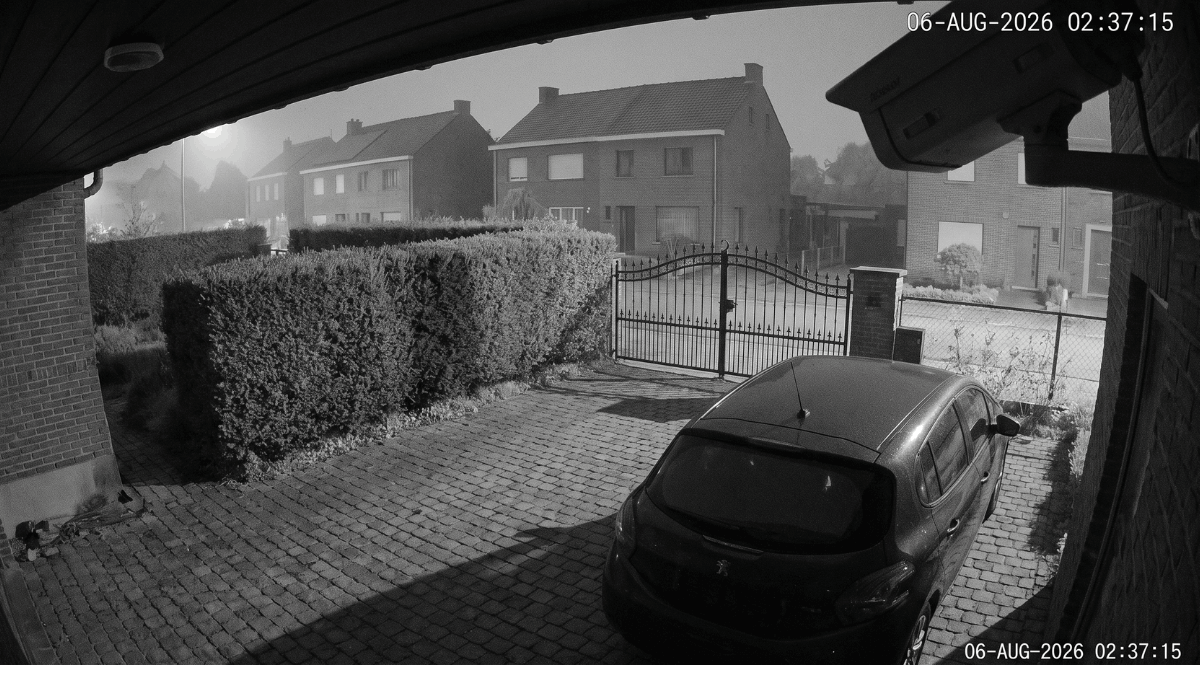 Een monochroom nachtzichtbeeld toont een Belgische oprit met een geparkeerde auto in fel infraroodlicht terwijl de achtergrond wegvalt in het donker.